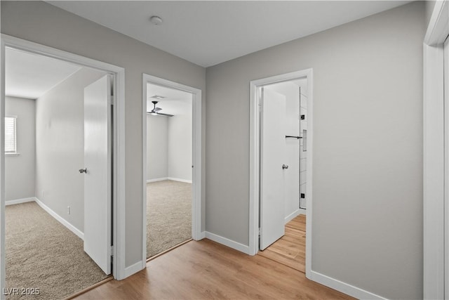 hallway featuring light carpet, light wood finished floors, and baseboards