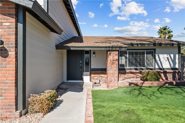 property entrance with a shingled roof, a lawn, and brick siding