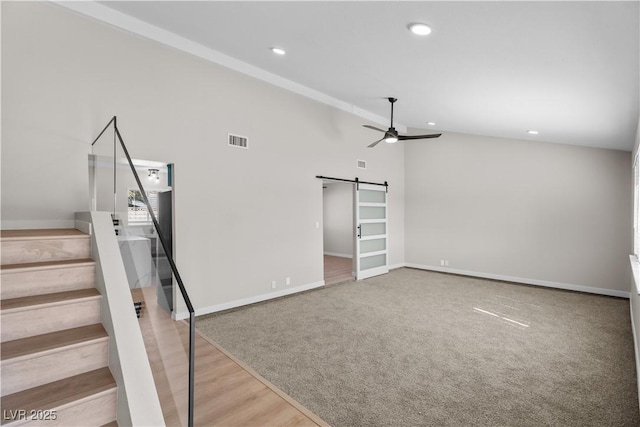 interior space featuring ceiling fan, a barn door, visible vents, vaulted ceiling, and stairway