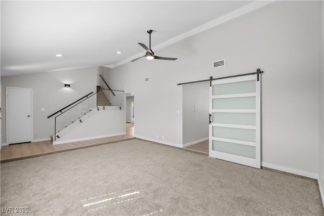 unfurnished living room featuring a barn door, carpet floors, visible vents, a ceiling fan, and stairs