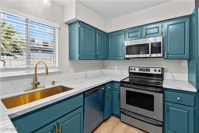 kitchen with light wood finished floors, light stone counters, stainless steel appliances, and a sink