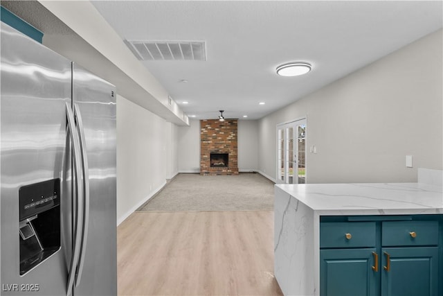 kitchen featuring visible vents, a brick fireplace, open floor plan, light stone countertops, and stainless steel fridge