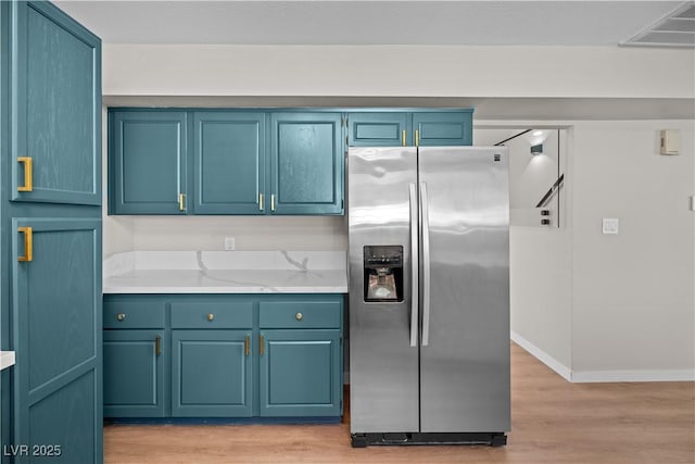 kitchen with light wood-type flooring, visible vents, light stone counters, and stainless steel fridge with ice dispenser