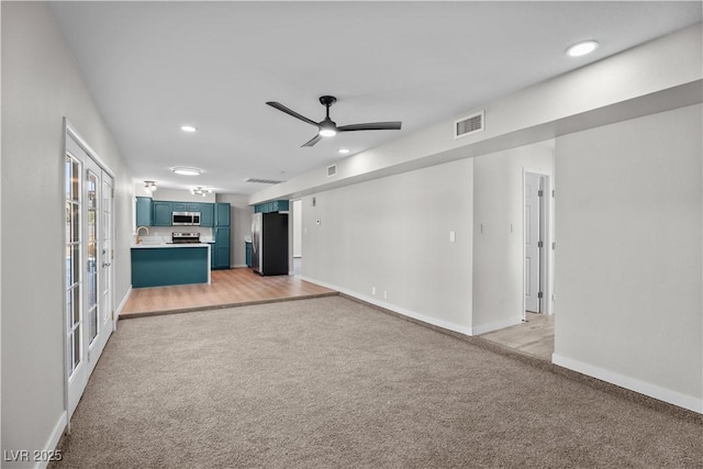 unfurnished living room featuring light colored carpet, ceiling fan, visible vents, and baseboards