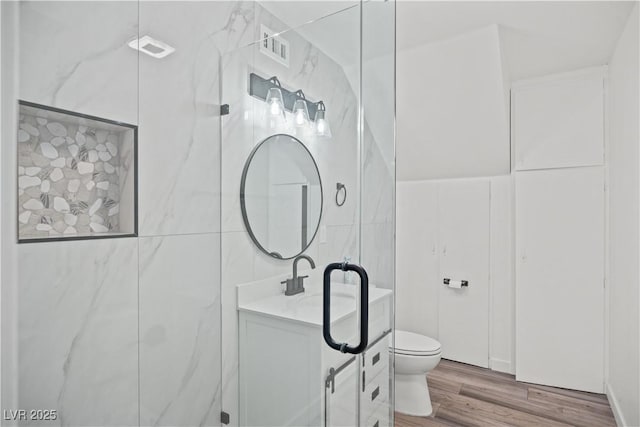 bathroom featuring visible vents, toilet, wood finished floors, vanity, and tile walls