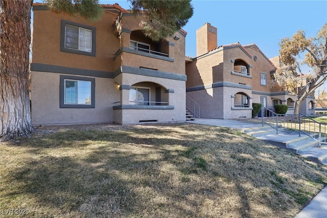 view of front of house featuring a front lawn, a balcony, and stucco siding