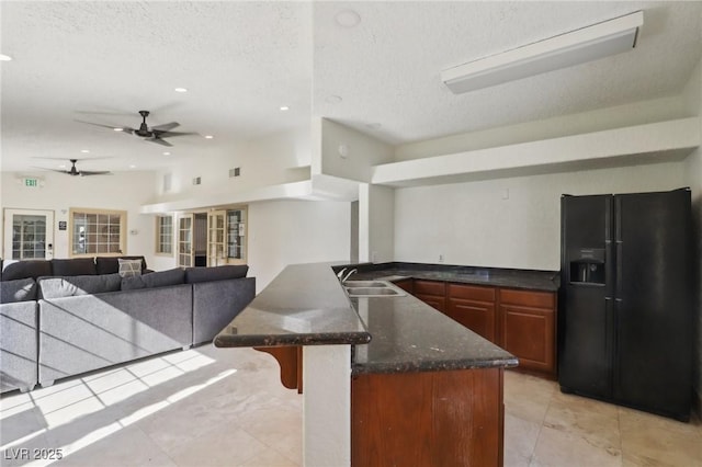 kitchen featuring dark stone counters, a breakfast bar, black refrigerator with ice dispenser, a textured ceiling, and a sink