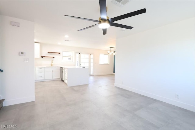 unfurnished living room with baseboards, visible vents, a sink, and ceiling fan with notable chandelier