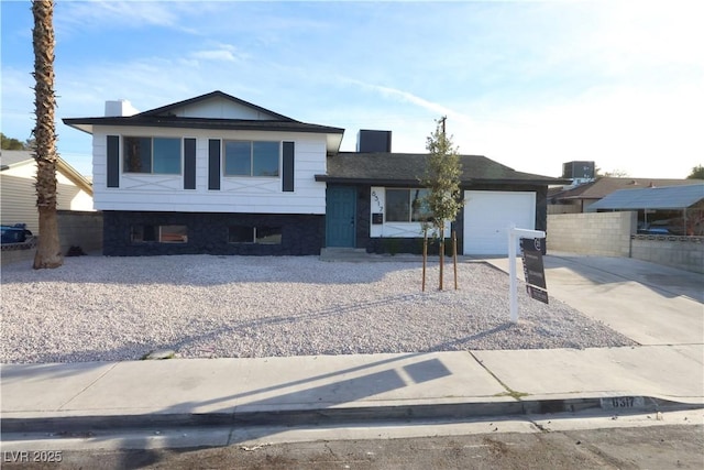 tri-level home with a garage, concrete driveway, a chimney, fence, and cooling unit