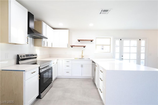 kitchen featuring visible vents, appliances with stainless steel finishes, a sink, a peninsula, and wall chimney exhaust hood