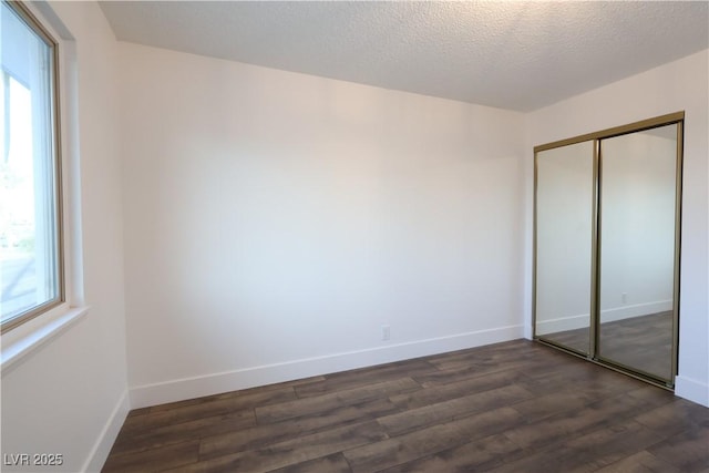 unfurnished bedroom featuring dark wood-style floors, multiple windows, a closet, and baseboards