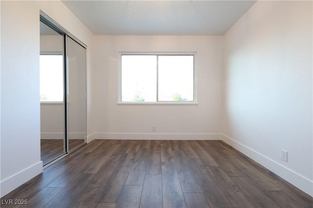 unfurnished bedroom with multiple windows, dark wood-style flooring, a closet, and baseboards