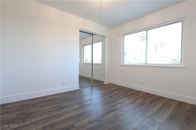 unfurnished bedroom featuring a textured ceiling, a closet, baseboards, and dark wood-style flooring