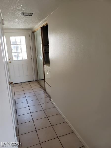 doorway featuring a textured ceiling, light tile patterned flooring, and baseboards