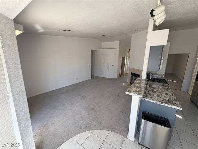 kitchen featuring lofted ceiling, light tile patterned floors, a textured ceiling, light colored carpet, and visible vents