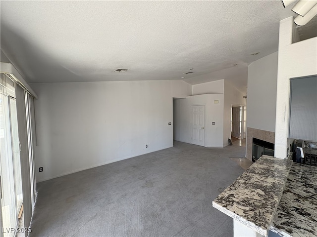 unfurnished living room featuring a fireplace, lofted ceiling, visible vents, carpet flooring, and a textured ceiling