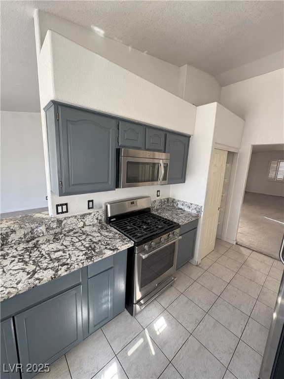 kitchen with light tile patterned floors, appliances with stainless steel finishes, light stone counters, and a textured ceiling