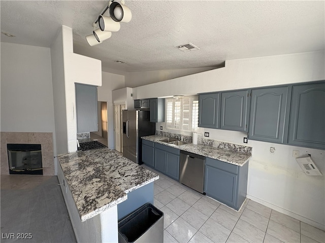 kitchen featuring a sink, visible vents, vaulted ceiling, appliances with stainless steel finishes, and a glass covered fireplace