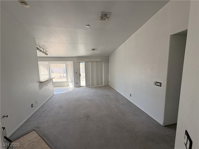 carpeted empty room with a textured ceiling, track lighting, visible vents, and baseboards