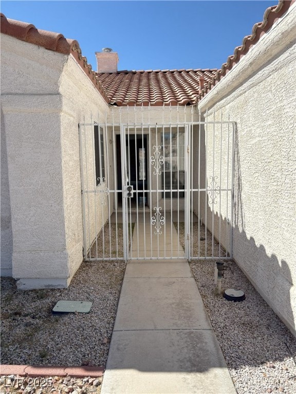 property entrance featuring a tile roof, a chimney, and stucco siding