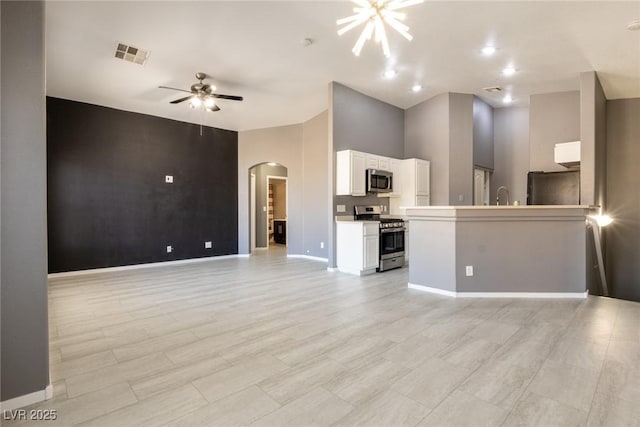 unfurnished living room featuring a ceiling fan, an accent wall, baseboards, visible vents, and arched walkways