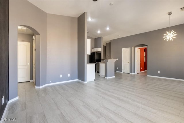 unfurnished living room featuring arched walkways, visible vents, and baseboards
