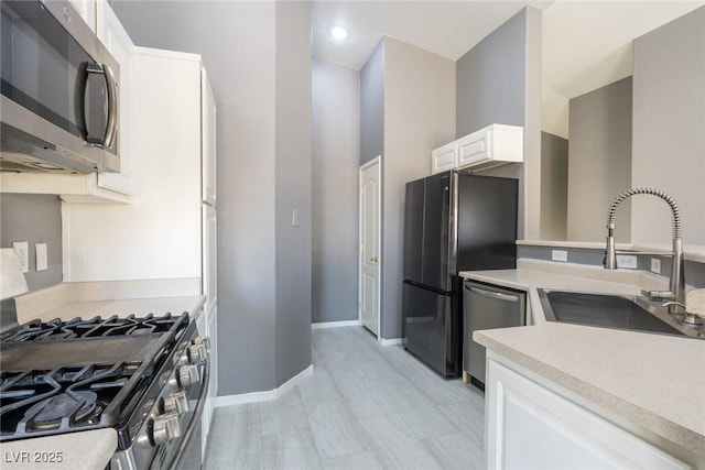 kitchen featuring light countertops, a sink, appliances with stainless steel finishes, baseboards, and white cabinets