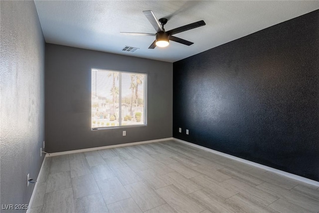 unfurnished room featuring a ceiling fan, a textured ceiling, baseboards, visible vents, and a textured wall
