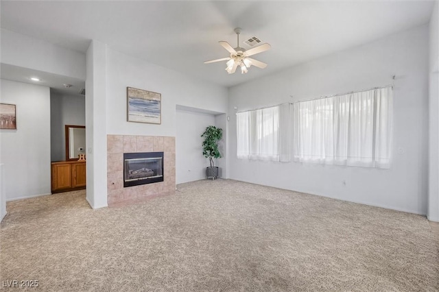 unfurnished living room featuring carpet, a tiled fireplace, visible vents, and a ceiling fan