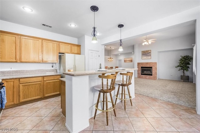 kitchen featuring visible vents, light carpet, light tile patterned flooring, white fridge with ice dispenser, and a kitchen breakfast bar