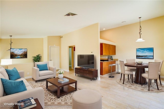 living area featuring vaulted ceiling, light wood finished floors, visible vents, and baseboards