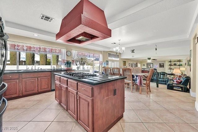 kitchen featuring a tray ceiling, light tile patterned flooring, a sink, stainless steel appliances, and dark countertops