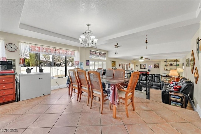 dining room featuring ceiling fan with notable chandelier, a tray ceiling, a textured ceiling, light tile patterned floors, and baseboards