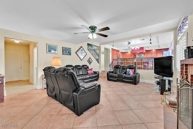 living area with ceiling fan with notable chandelier, a tray ceiling, stairway, light tile patterned flooring, and baseboards