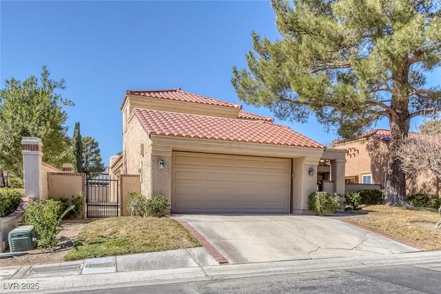 mediterranean / spanish-style home with an attached garage, a tiled roof, concrete driveway, a gate, and stucco siding