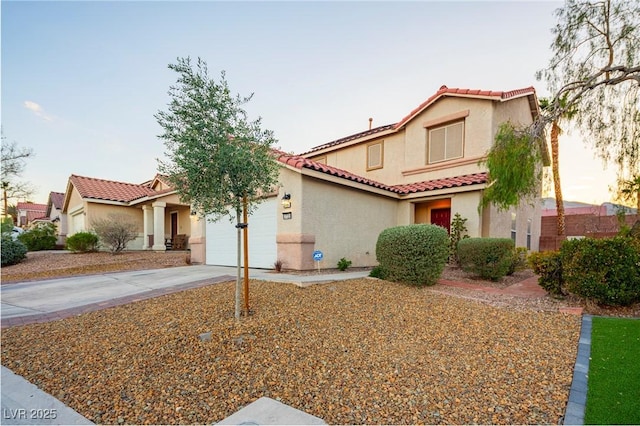 mediterranean / spanish house with a garage, a tile roof, concrete driveway, and stucco siding