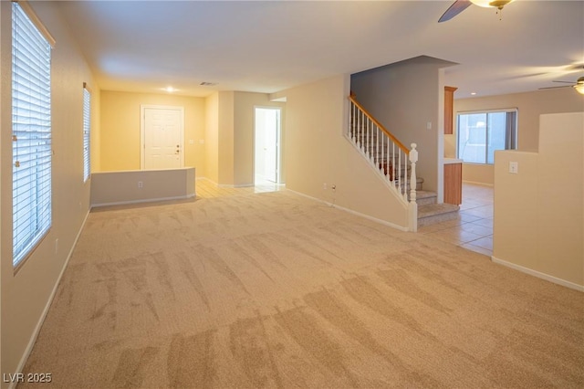 spare room featuring ceiling fan, carpet floors, baseboards, stairs, and tile patterned floors