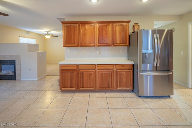 kitchen featuring light tile patterned floors, stainless steel fridge, decorative backsplash, a tiled fireplace, and a ceiling fan