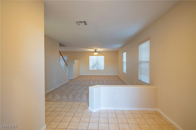 empty room with light carpet, light tile patterned floors, visible vents, a ceiling fan, and stairway