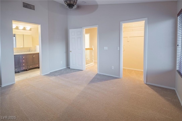 unfurnished bedroom featuring light carpet, ensuite bath, a spacious closet, and visible vents