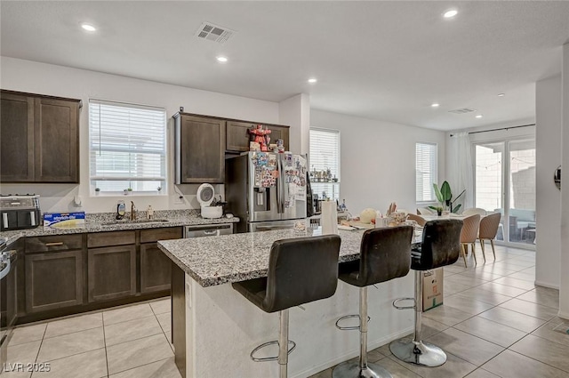 6747 Marjoram St, Las Vegas, NV 89166 - kitchen with stainless steel refrigerator with ice dispenser, a sink, light stone counters, a kitchen bar, and light tile patterned floors