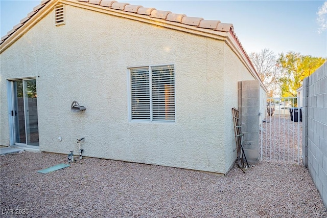 view of side of home with fence, a tiled roof, and stucco siding