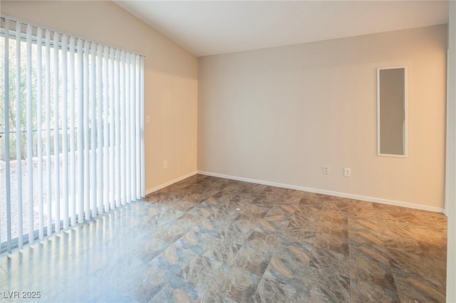 spare room featuring vaulted ceiling, stone finish floor, and baseboards