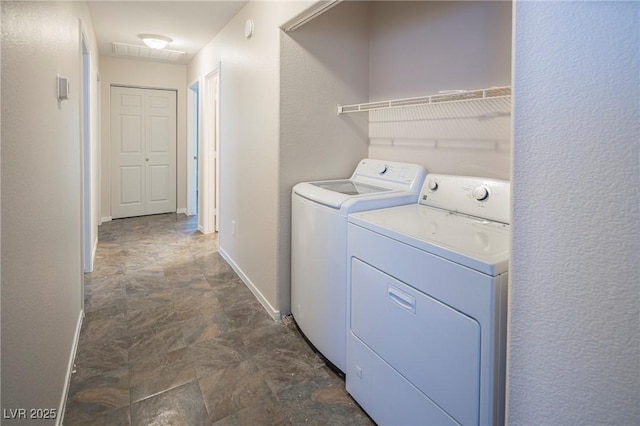 laundry room with laundry area, stone finish flooring, baseboards, and separate washer and dryer