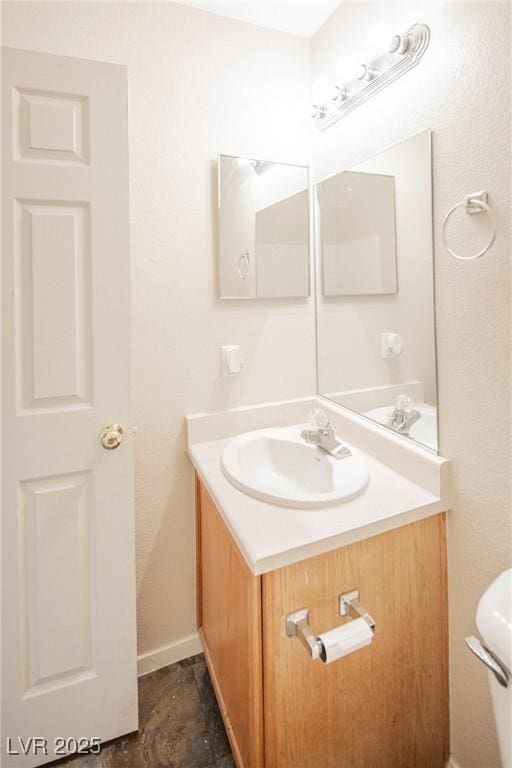 bathroom with toilet, vanity, and baseboards