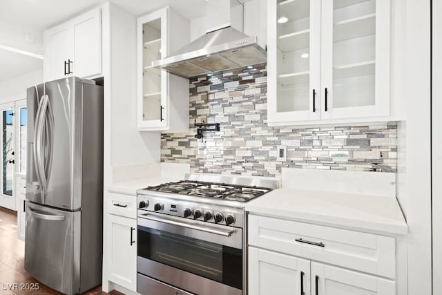 kitchen featuring decorative backsplash, appliances with stainless steel finishes, glass insert cabinets, white cabinets, and wall chimney exhaust hood