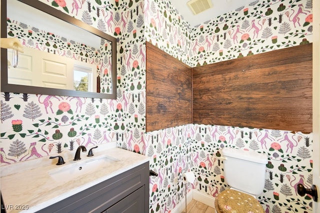 half bathroom featuring toilet, wallpapered walls, visible vents, and vanity