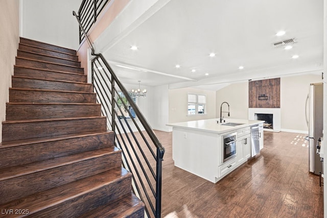 kitchen featuring a fireplace, stainless steel appliances, visible vents, open floor plan, and a sink