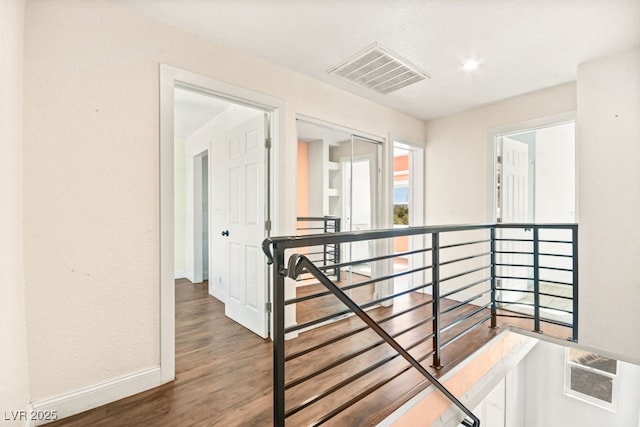 corridor featuring baseboards, visible vents, an upstairs landing, and wood finished floors