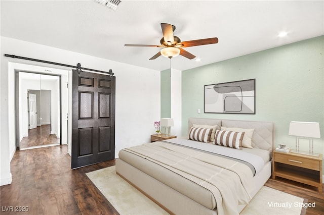 bedroom with a barn door, dark wood-style flooring, visible vents, and a ceiling fan